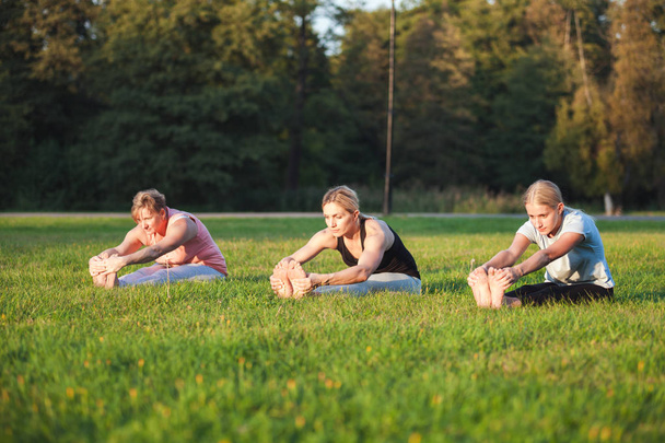 Yoga en el parque, grupo de mujeres de edad mixta haciendo pose mientras se pone el sol - Foto, Imagen
