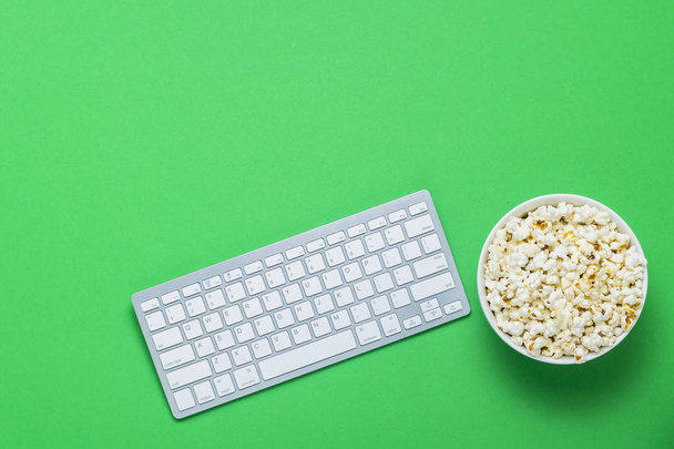 Toetsenbord en kom met popcorn op een groene achtergrond. Het concept van het bekijken van films, Tv-shows, shows, sport online. Plat lag, top uitzicht - Foto, afbeelding