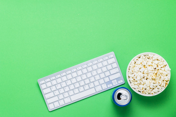 Näppäimistö, tölkki juomalla ja kulhollinen popcornia vihreällä taustalla. Käsite katsomassa elokuvia, TV-ohjelmia, ohjelmia, urheilu verkossa. Tasainen, ylhäältä
 - Valokuva, kuva