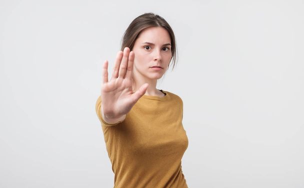 Vakava nuori eurooppalainen nainen seisoo ojennetulla kädellä osoittaa stop ele eristetty valkoisella taustalla
 - Valokuva, kuva