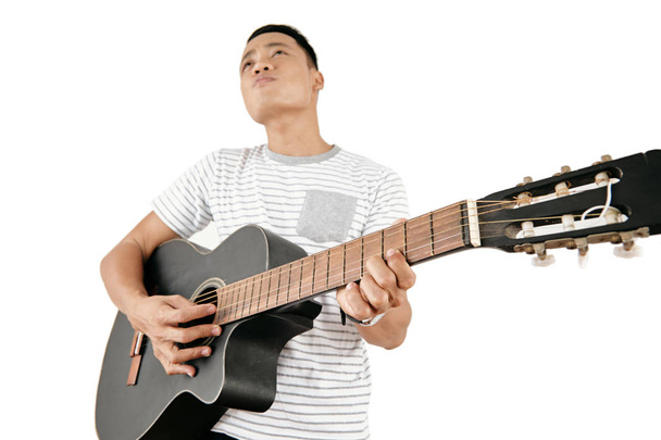 Retrato de un joven asiático con camiseta casual tocando la guitarra sobre fondo blanco, vista de bajo ángulo
 - Foto, imagen