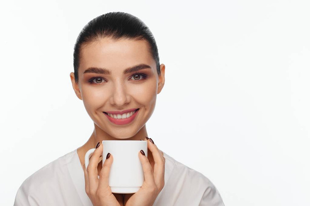 Portrait of a smiling beautiful woman with collected hair and a white mug in her hands. White background - Zdjęcie, obraz