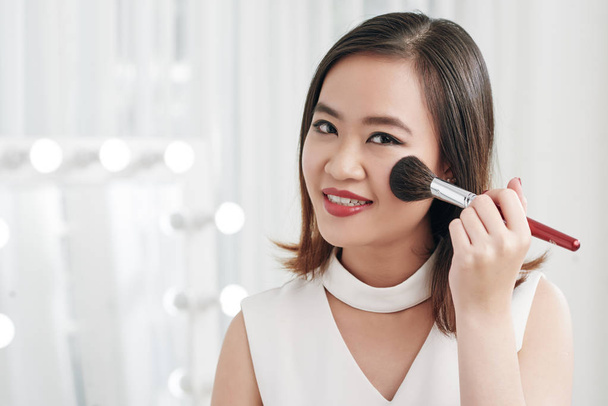 Smiling young Asian woman applying powder blush - Foto, afbeelding
