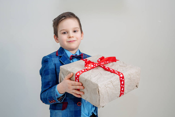 Adorable boy in suit with a gift box on a light background, st valentines day concept - Фото, изображение