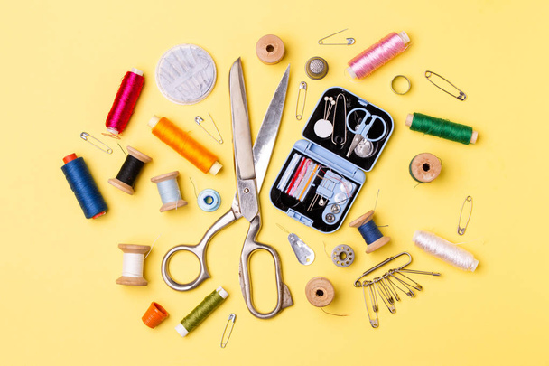 Composition with threads and sewing accessories - scissors, centimeter, pins on yellow background. - Фото, зображення
