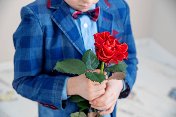 Little boy in suit standing with red rose, on a light background, st. valentine's day concept - Photo, Image