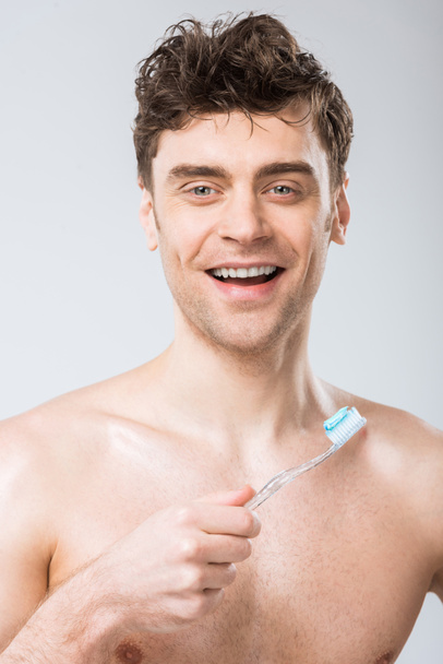smiling man holding toothbrush with toothpaste, isolated on grey - Foto, afbeelding