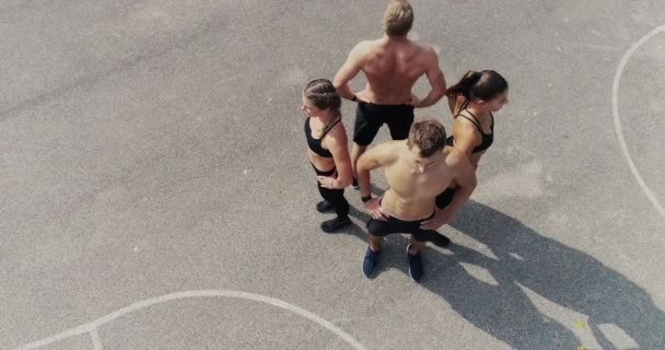 τέσσερις νέοι γυμναστήριο αθλητές στέκεται πλάτη με πλάτη στο γήπεδο στην ηλιόλουστη μέρα  - Πλάνα, βίντεο