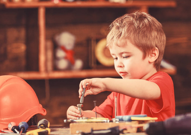 Toddler on busy face plays with bolts at home in workshop. Kid boy play as handyman. Child cute and adorable playing with bolts as builder or repairer, repairing or handcrafting. Handcrafting concept - Photo, Image