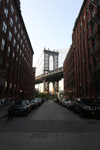 On the street on the sides there are houses and there are a lot of cars. Manhattan bridge background - Foto, afbeelding