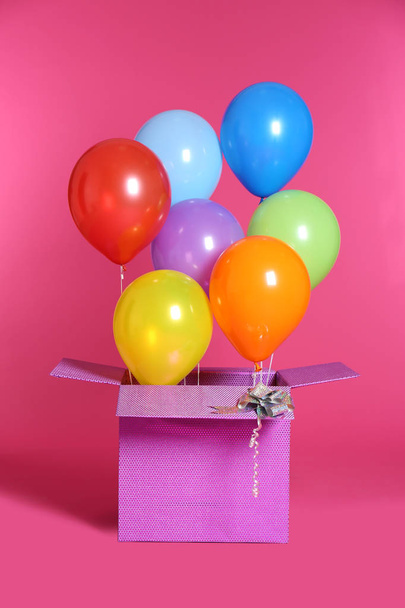 Gift box with bright air balloons on color background - Foto, afbeelding