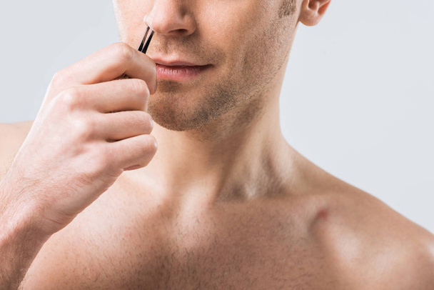cropped view of man plucking hair with tweezers from nose, isolated on grey - Foto, Imagen