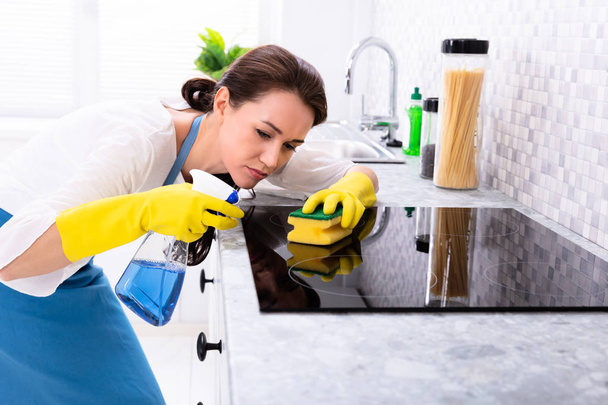 Young Woman Cleaning Induction Stove With Sponge In Kitchen - Valokuva, kuva