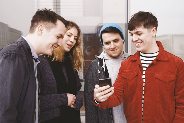 joven mostrando algo divertido en su teléfono inteligente a un grupo de amigos - adolescentes urbanos divirtiéndose y riendo juntos
 - Foto, Imagen