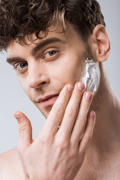 handsome macho applying shaving foam on face, isolated on grey - Zdjęcie, obraz