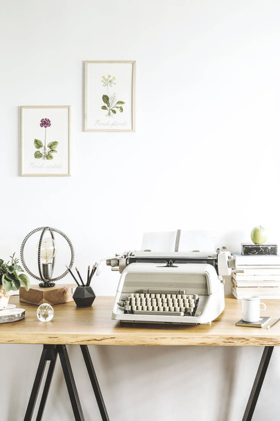 Stylish home office. Concept of inspirational home office interior with wooden desk and vintage typewriter. Composition of books, vintage illustrations of plants, lamp and office accessories.  - Zdjęcie, obraz