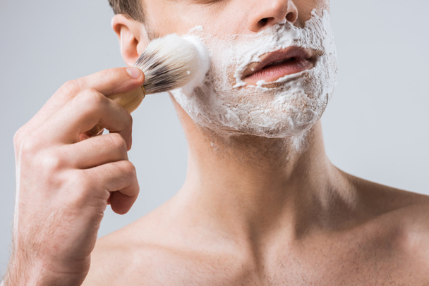 cropped view of young man applying shaving foam with brush, isolated on grey - Foto, imagen