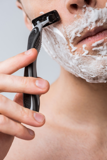 cropped view of young man foam on face shaving with razor, isolated on grey - Fotografie, Obrázek