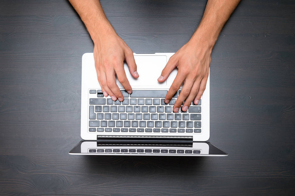 Ein Mann arbeitet mit einem Laptop auf einem Holztisch. Hände tippen auf einer Tastatur. von oben, Büroarbeitsplatz - Foto, Bild