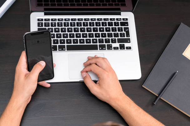 Antika ahşap masa dizüstü bilgisayar üzerinde çalışırken akıllı telefon yazarak eller mans. Tipik bir klavye üzerinde eller. Üstten görünüm, iş Ofis İşyeri - Fotoğraf, Görsel