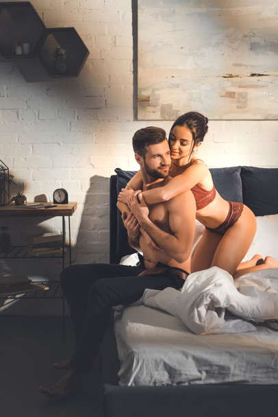 beautiful sexy woman embracing shirtless man on bed at home - Photo, Image