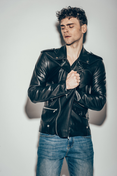 handsome sexy man posing in black leather jacket on grey - Foto, imagen