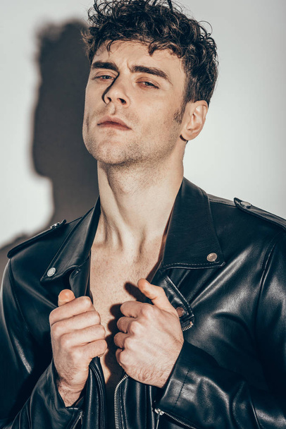 portrait of sexy man posing in black leather jacket on grey - Photo, Image