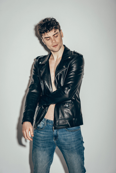 stylish sexy rocker posing in black leather jacket on grey - Фото, изображение