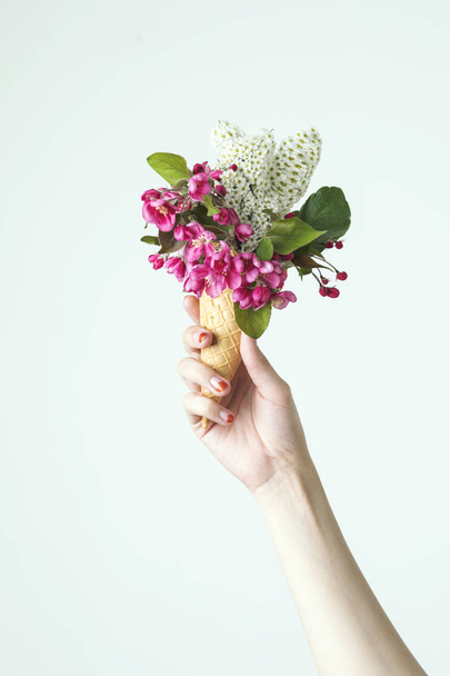 Woman holding in hand bouquet of pink and white flowers in waffle cone on light background - Foto, imagen
