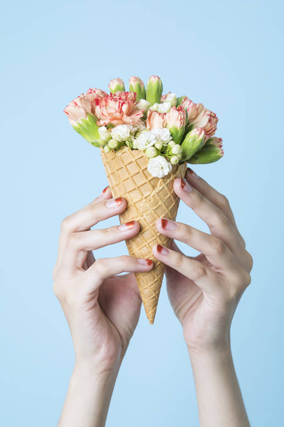 Female hands holding carnation bouquet in waffle cone on pastel blue background  - 写真・画像