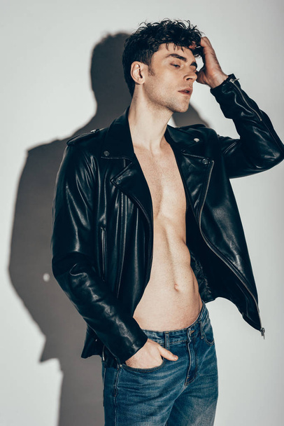 handsome sexy man posing in jeans and black leather jacket on grey - Foto, imagen
