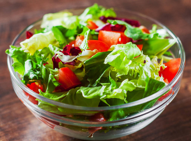 diverses feuilles de salade mélange frais avec tomate dans un bol en verre sur fond en bois
. - Photo, image