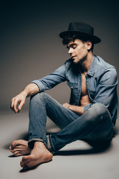 handsome sexy man posing in denim clothes and trendy hat on dark grey - Photo, Image