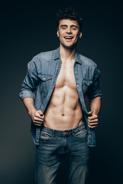 happy muscular man posing in denim clothes isolated on dark grey - Photo, Image