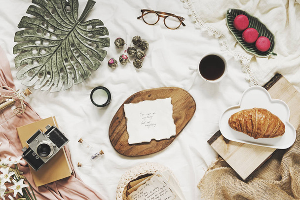 Trendy flat lay of workplace in bed with card, woman accessories and retro photo camera. Lifestyle blogg concept. - 写真・画像