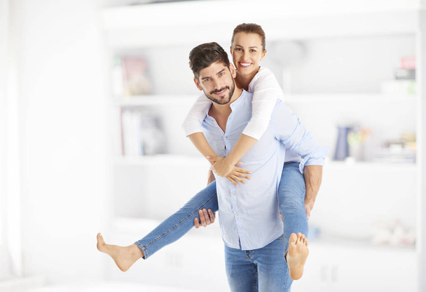 Shot of a happy young couple having fun. Handsome young man giving piggyback to her beautiful girlfriend while standing at home. - Foto, afbeelding