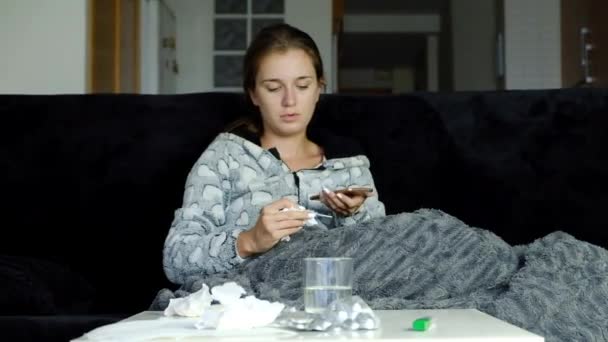 Young sick woman with fever talking on the cell phone with her doctor and taking pills. - Séquence, vidéo