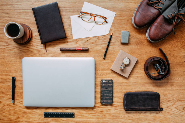 Stylish and modern composition of wooden desk with laptop, phone, shoes notebook, glasses and office accessories. Creative desk of traveler. - Photo, Image