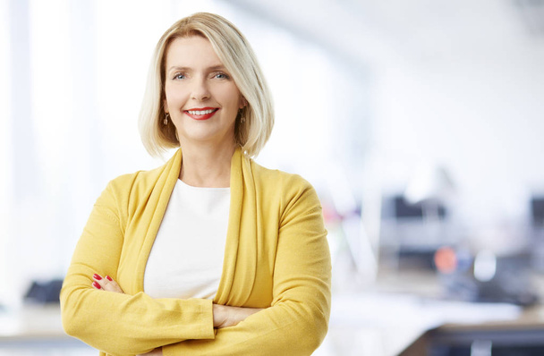 A beautiful mature sales businesswoman wearing casual clothes and smiling to you while standing with arms crossed at the office.  - Fotoğraf, Görsel