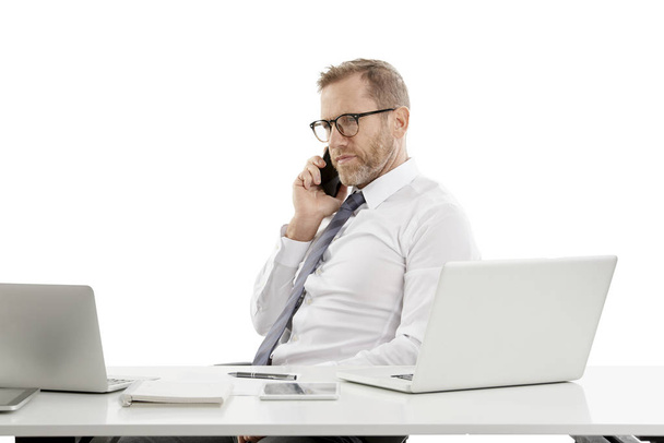 Portrait of a middle aged businessman looking thoughfully while sitting at desk and making call and working on laptop.  - Foto, Imagen