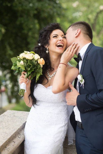Жінка і чоловік посміхаються в день весілля. Наречений цілує щасливу наречену з букетом. Весільна пара закохана. Молода пара влітку на свіжому повітрі. Концепція шлюбу. любов і сім'я
 - Фото, зображення