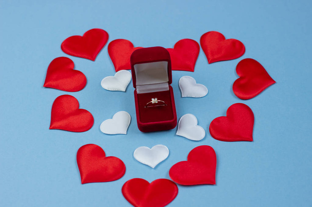 The ring in the red box on the background of hearts of red and white. Wedding ring in the box. Marriage proposal concept, Valentine's Day, International Women's Day. - Фото, зображення