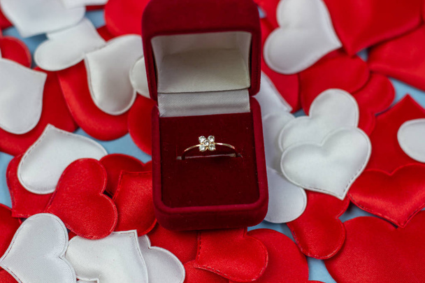 Ring in einem roten Kasten auf rotem und weißem Hintergrund. Ehering in der Box. Heiratsantrag-Konzept, Valentinstag, internationaler Frauentag. - Foto, Bild