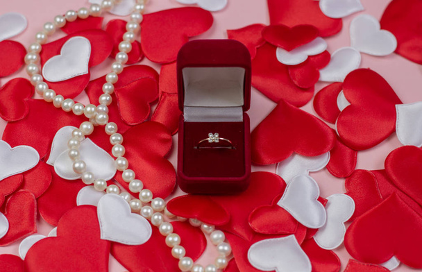 Ring in a red box and pearls on a background of hearts of red and white. Wedding ring in the box. Marriage proposal concept, Valentine's Day, International Women's Day. - Фото, зображення