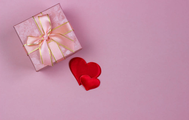 Ένα δώρο σε ένα όμορφο κουτί και κόκκινες καρδιές σε ροζ φόντο. Ημέρα του Αγίου Βαλεντίνου, ημέρα της γυναίκας. - Φωτογραφία, εικόνα