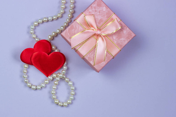 A gift in a pink box with pearls and valentines on a purple background. Valentine's Day and International Women's Day - Foto, immagini