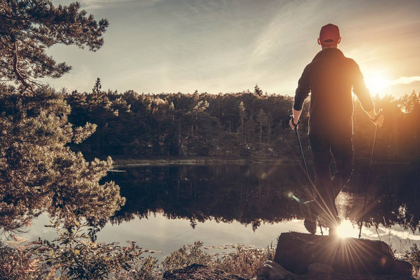 Caucasian Hiker and Scenic Lake Sunset. Men with Nordic Walking Poles Taking a Moment on the Lake Shore. - Fotó, kép