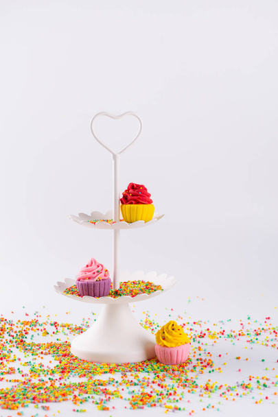 Branco bandeja de serviço de duas camadas e cupcakes de açúcar multicoloridos em miniatura com polvilhas
 - Foto, Imagem