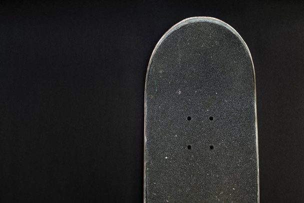 Parte superior delantera de una tabla de skate con cinta de agarre y agujeros de perno sobre fondo negro
 - Foto, Imagen