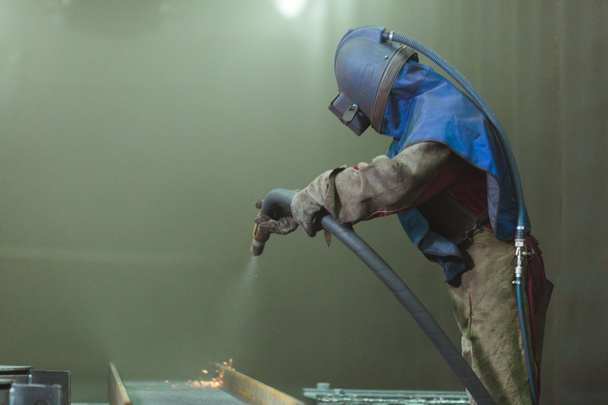Zandstraal. Metaal stralen. Een werknemer bereidt een metalen onderdeel voor om te schilderen. Een harde man werkt in de fabriek. - Foto, afbeelding